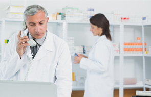 Pharmacist on the phone standing in a pharmacy with another pharmacist